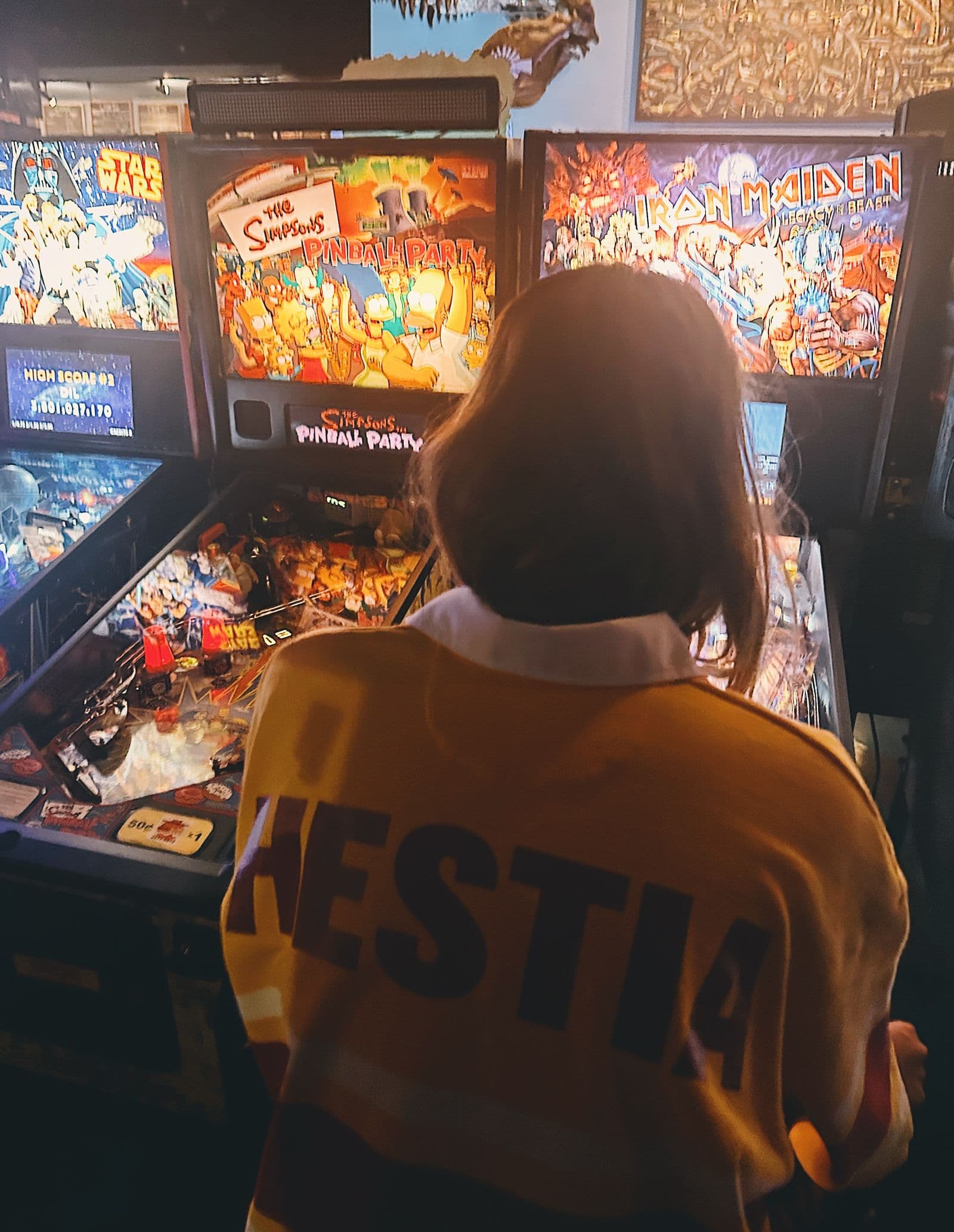 Someone in a Hestia jacket playing a pinball machine